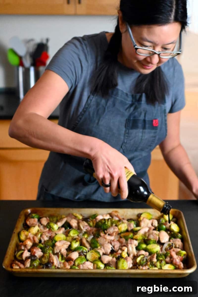 One Pan Chicken and Crispy Brussels Bake 11 A person drizzling aged balsamic vinegar over the freshly roasted chicken and vegetables on the sheet pan, adding a final, enhancing touch.