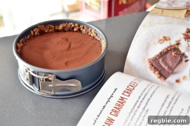 Paleo Vegan Gluten Free Chocolate Graham Cracker Pie 5 A small, perfectly formed paleo chocolate pie in a springform pan, positioned beside 'The Paleo Chocolate Lovers' Cookbook,' ready to be chilled or served.