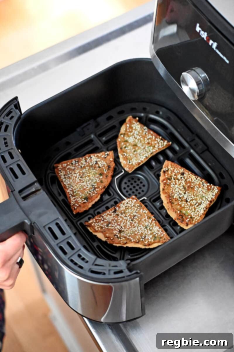 Wholesome Paleo Shrimp Toast 18 A hand holding an air fryer open, revealing four golden brown, crispy wedges of paleo shrimp toast inside the basket, just cooked.