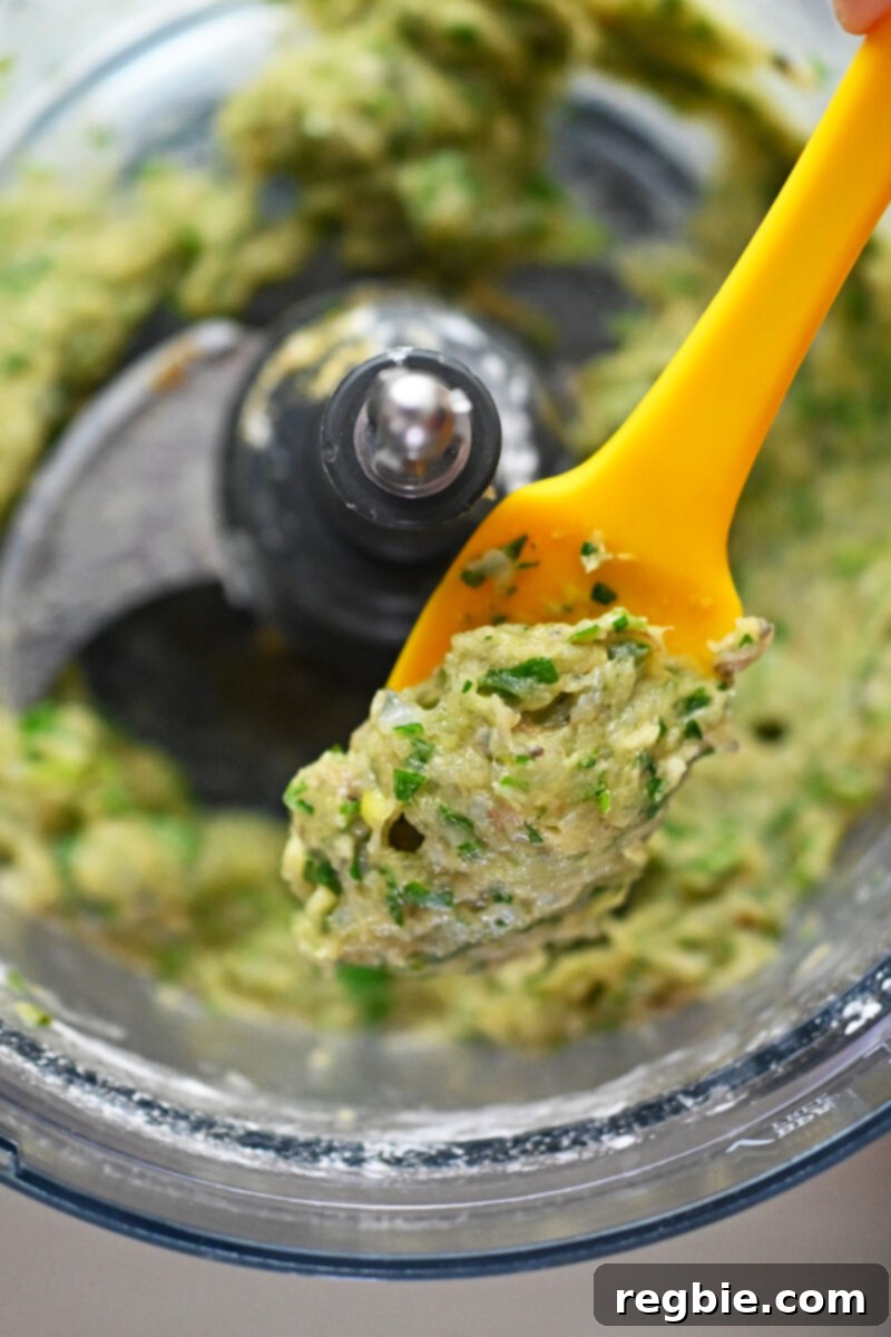 Wholesome Paleo Shrimp Toast 7 Close-up shot of a yellow silicone spatula lifting some perfectly blended shrimp paste from an open food processor bowl.
