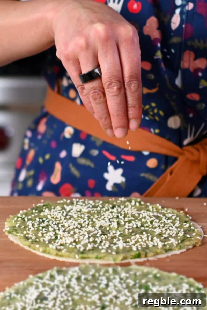 Wholesome Paleo Shrimp Toast 10 Hands sprinkling white sesame seeds evenly on tortillas topped with a thin layer of raw shrimp paste.