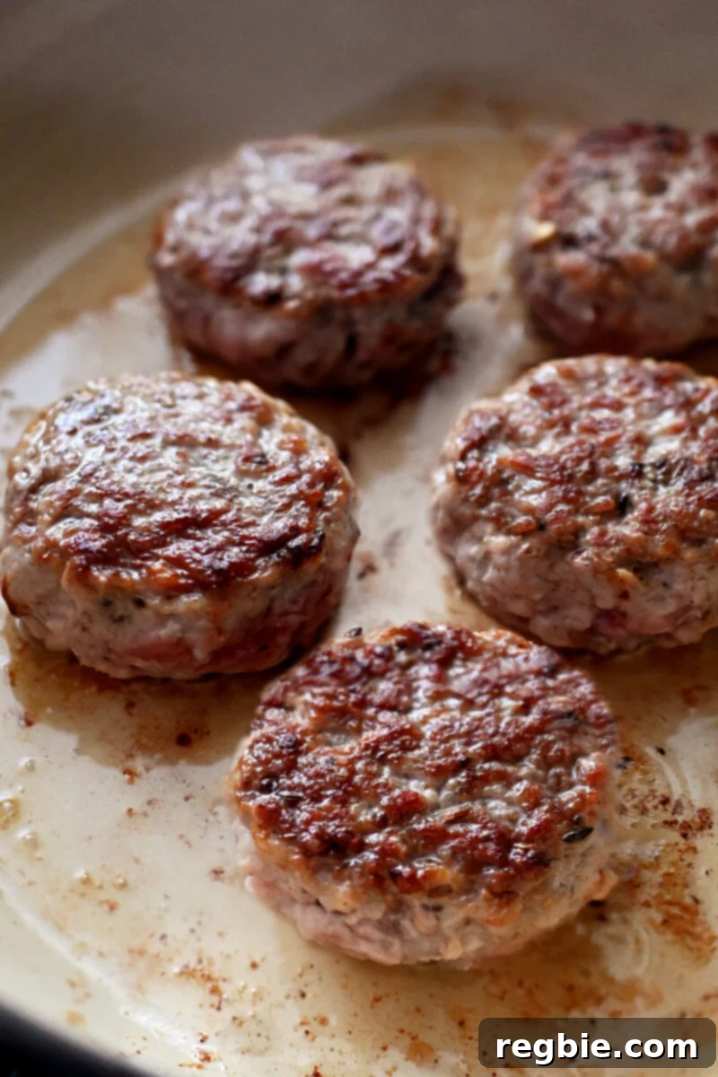 An enamel cast iron skillet filled with golden brown sausage patties.