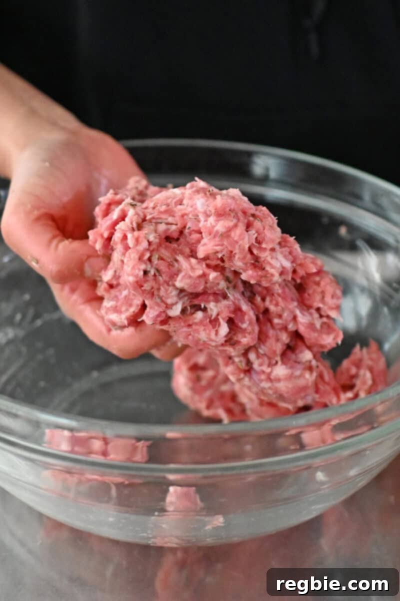A hand is mixing homemade Whole30 Italian sausage in a clear glass bowl.