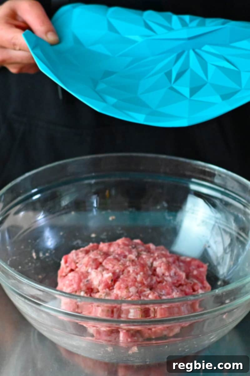 Two hands are placing a blue silicone lid on a bowl of raw Italian sausage that will be stored in the fridge.