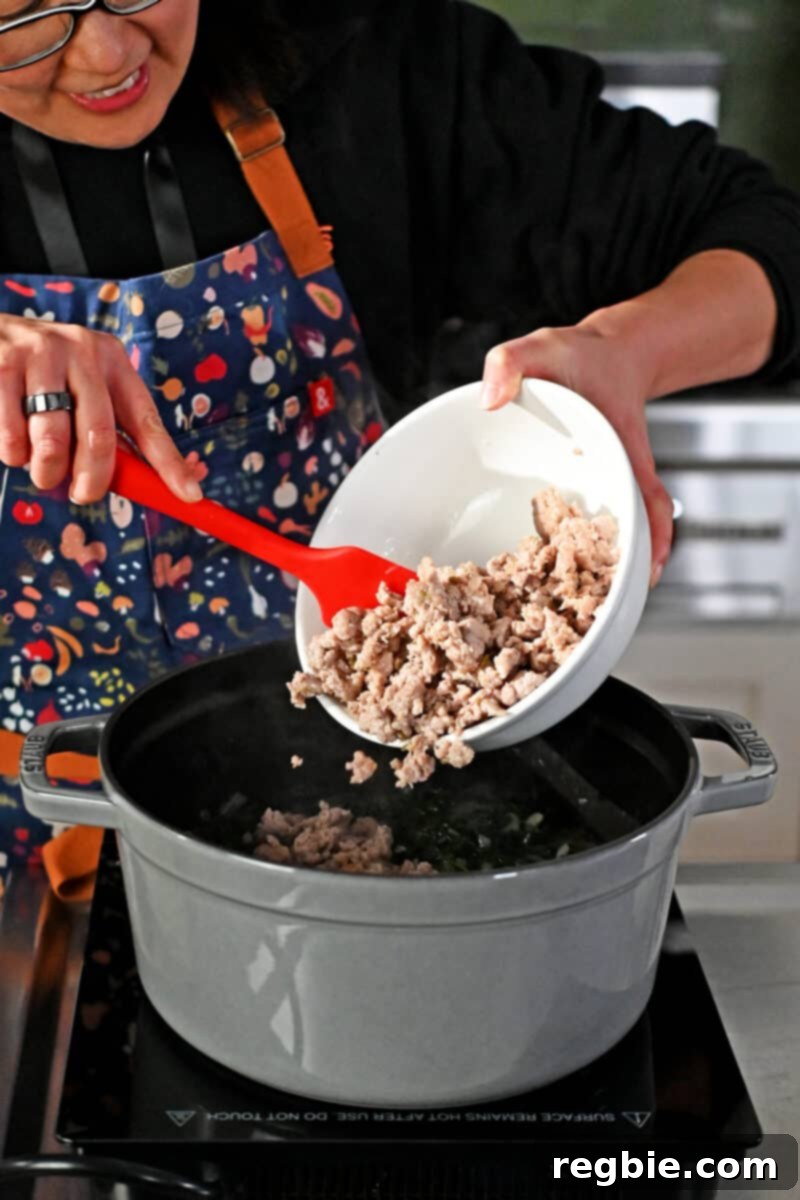 Adding cooked bulk Italian sausage into a pot of Zuppa Toscana.