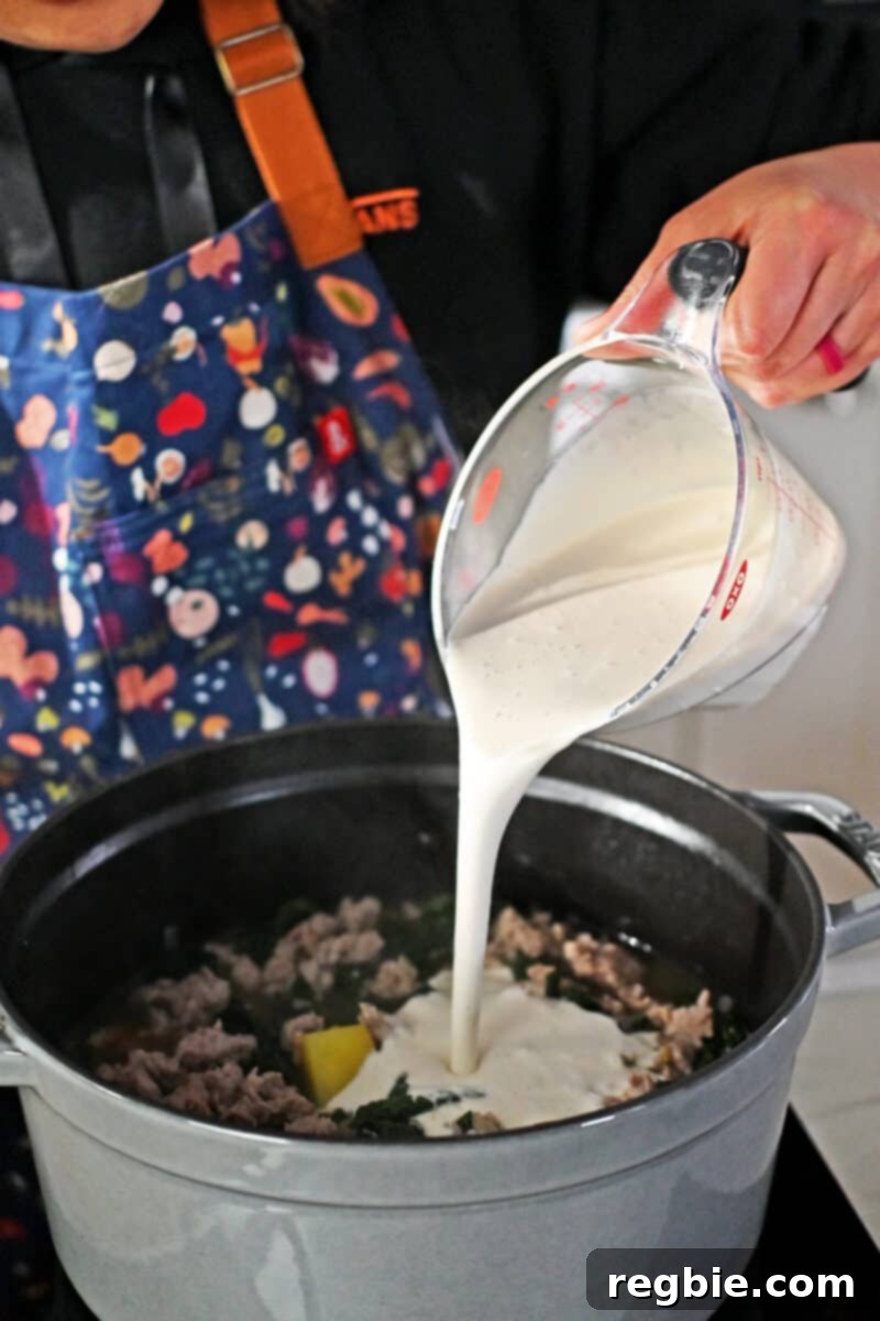 Pouring cashew cream into a pot filled with Zuppa Toscana.