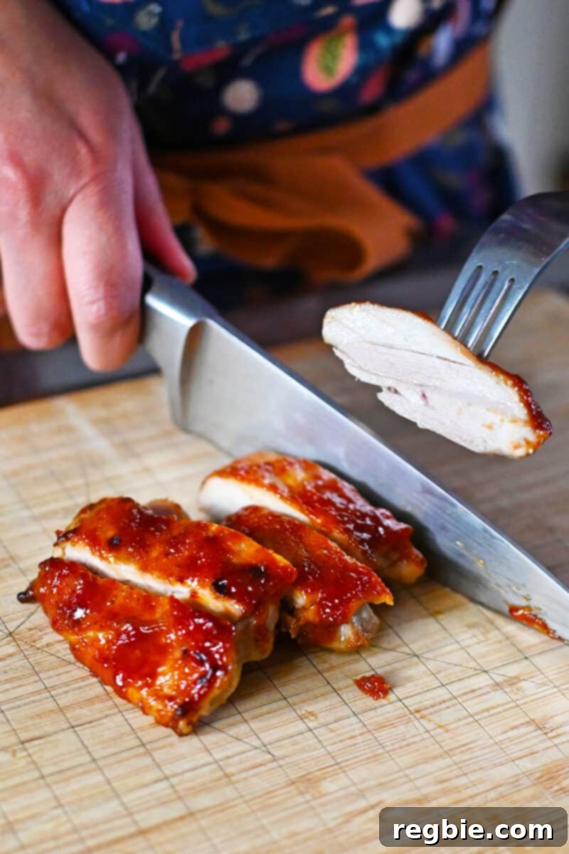 A piece of Char Siu chicken being sliced on a cutting board, with a fork holding up a piece to show its tender interior.