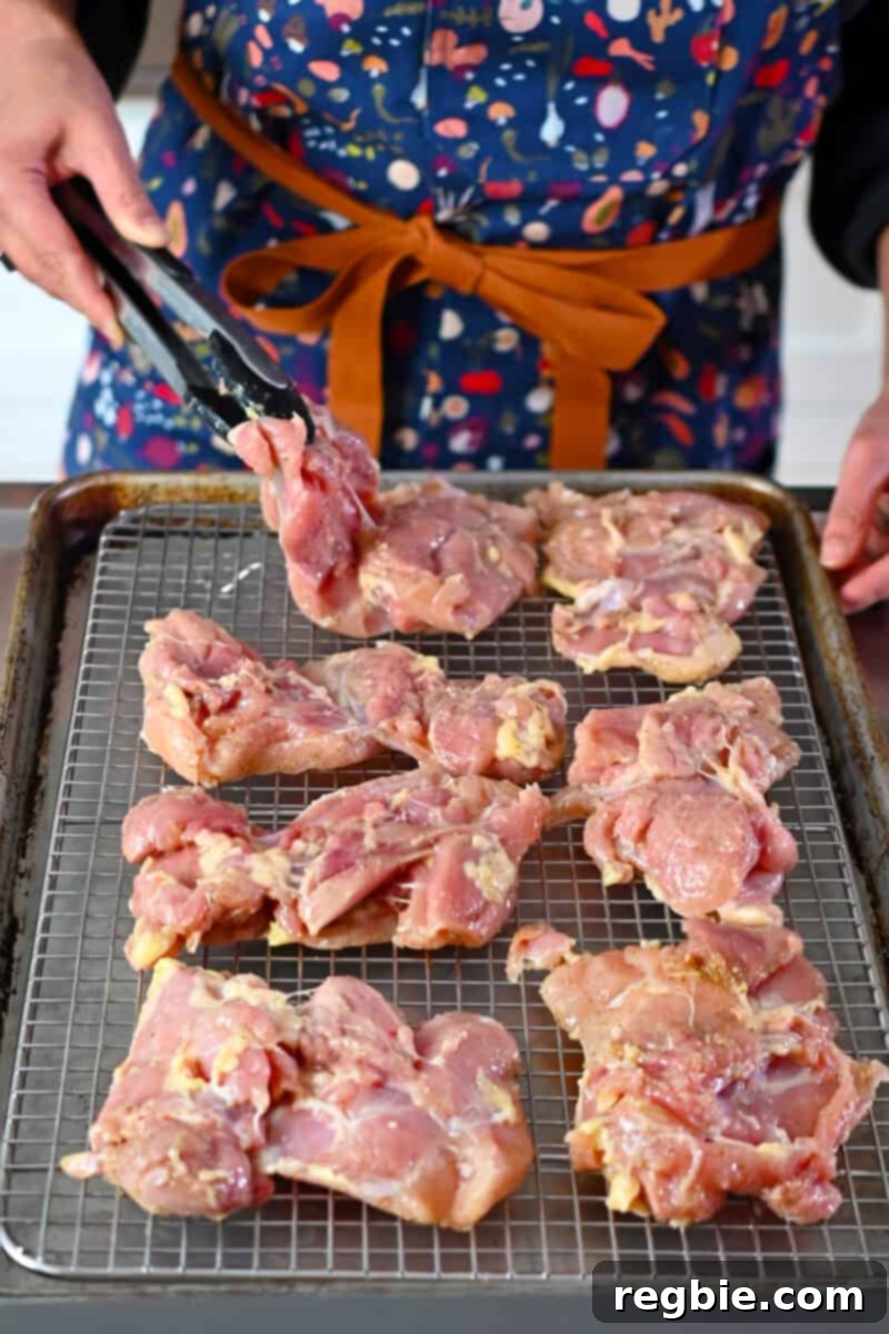 Placing boneless skinless chicken thighs on a wire rack in a rimmed baking sheet, arranged in a single layer for even cooking.