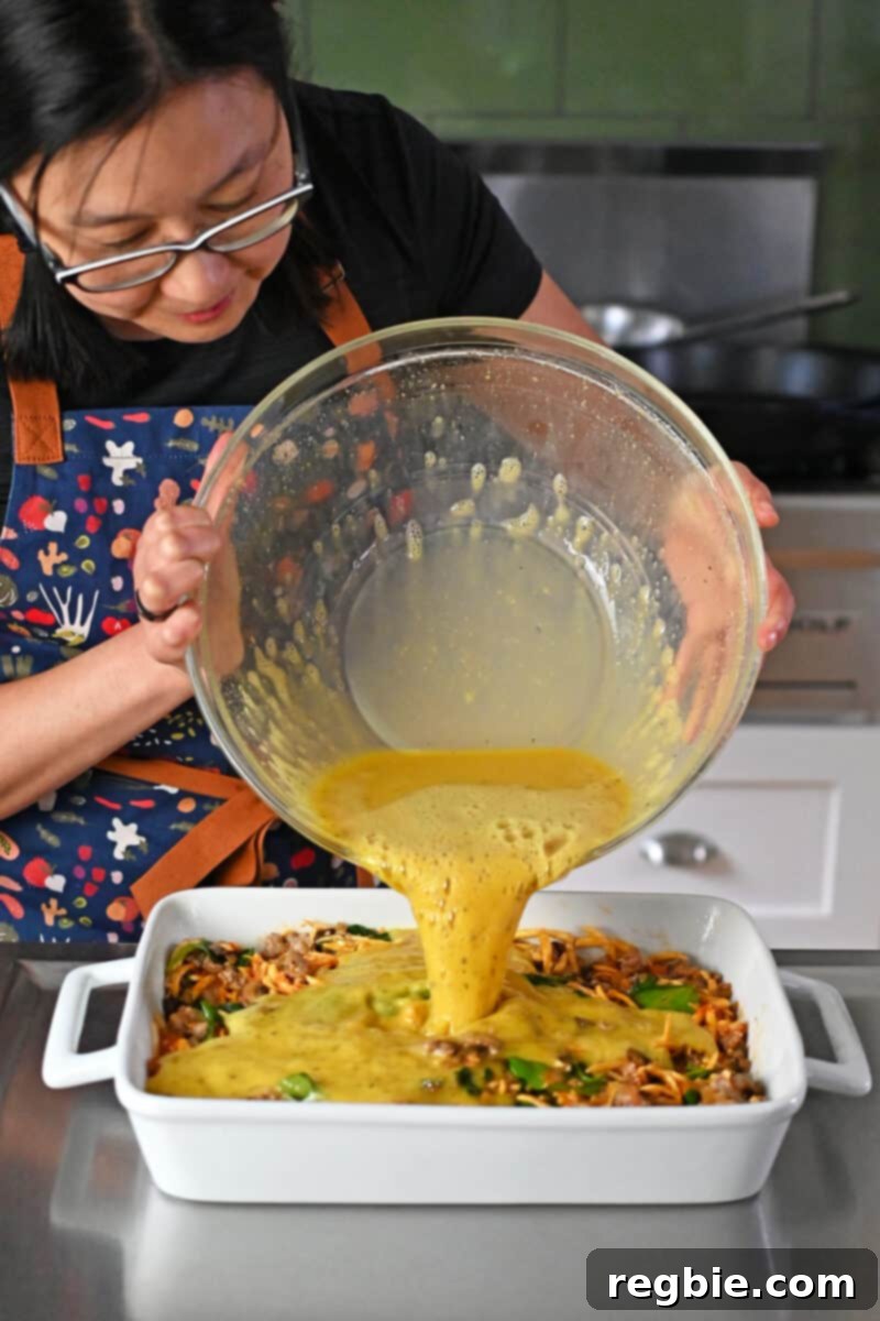 Skillfully pouring the perfectly seasoned, whisked raw eggs into a casserole pan already filled with the delicious sausage and vegetable base, ready for baking.