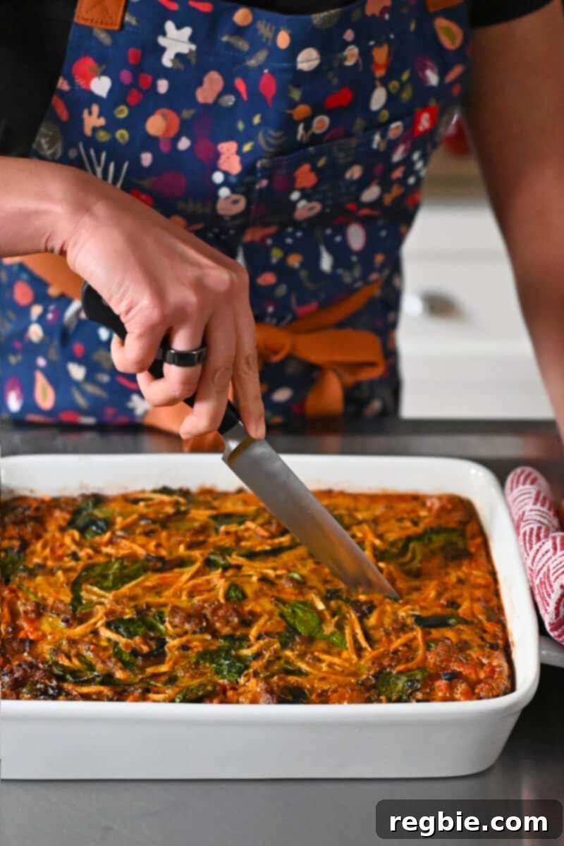 Expertly slicing a hearty paleo and Whole30 sausage breakfast casserole into perfect portions, ready to be served and enjoyed.