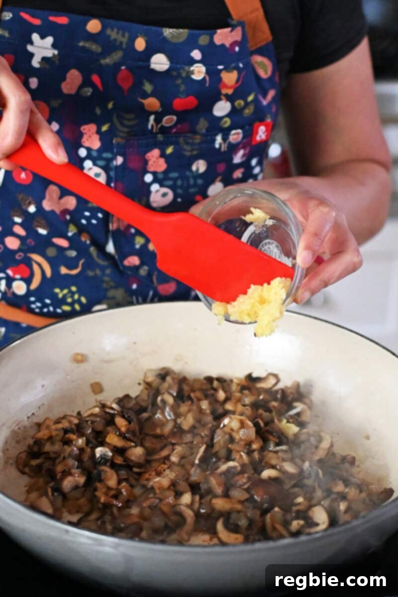 Adding aromatic minced garlic to a skillet already filled with perfectly sautéed mushrooms and onions, enhancing the savory base of the casserole.