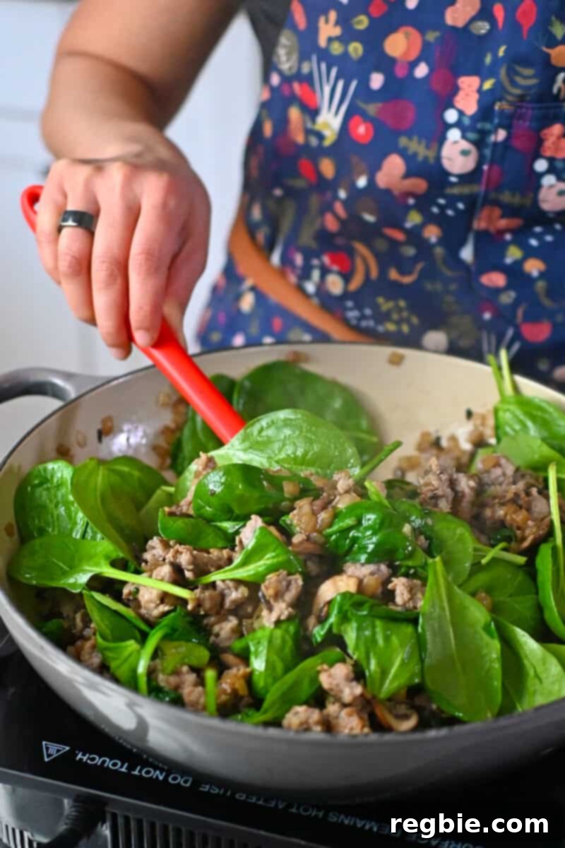 Vigorously stirring fresh baby spinach into a skillet brimming with cooked mushrooms, onions, and flavorful Italian sausage, allowing the greens to just begin wilting.