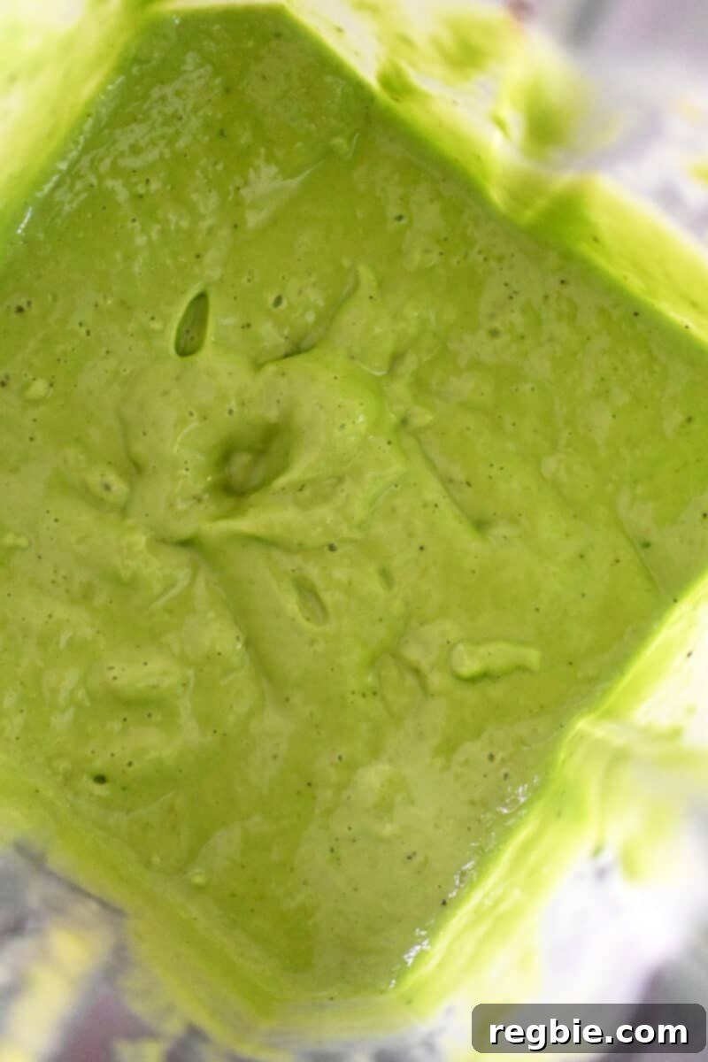 An overhead shot of an open Vitamix blender, revealing a perfectly smooth and bright green Green Goddess Dressing inside, ready to be poured.