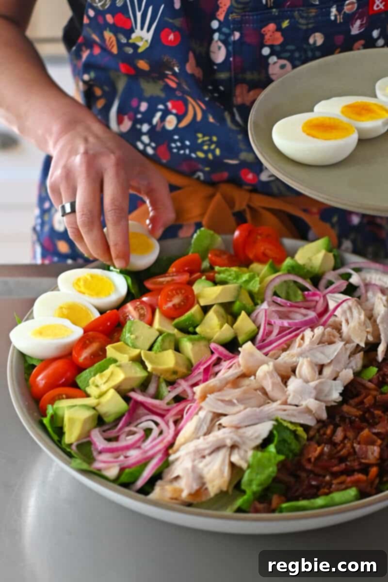 Carefully placing halved hard-boiled eggs in a row on a Cobb salad, alongside other fresh ingredients.