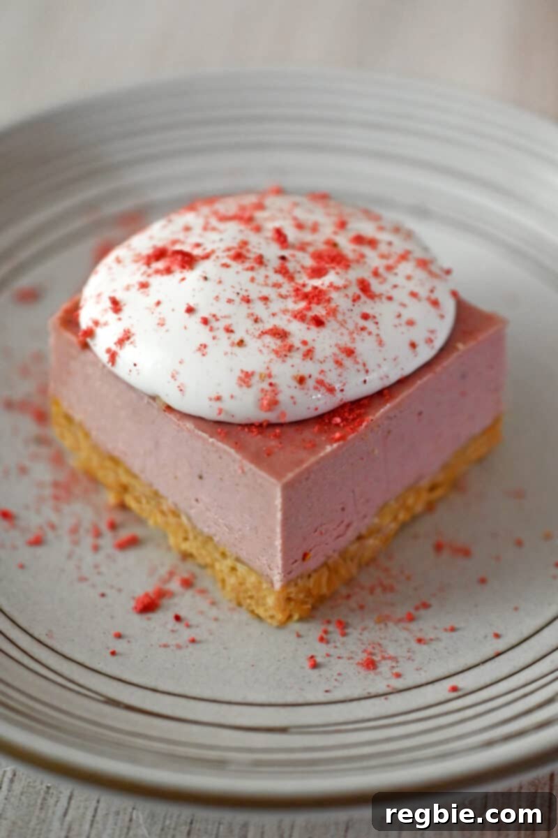 A beautifully presented slice of paleo, vegan, and gluten-free strawberry cheesecake bar on a white plate, elegantly topped with fluffy whipped coconut cream and a dusting of vibrant strawberry powder.