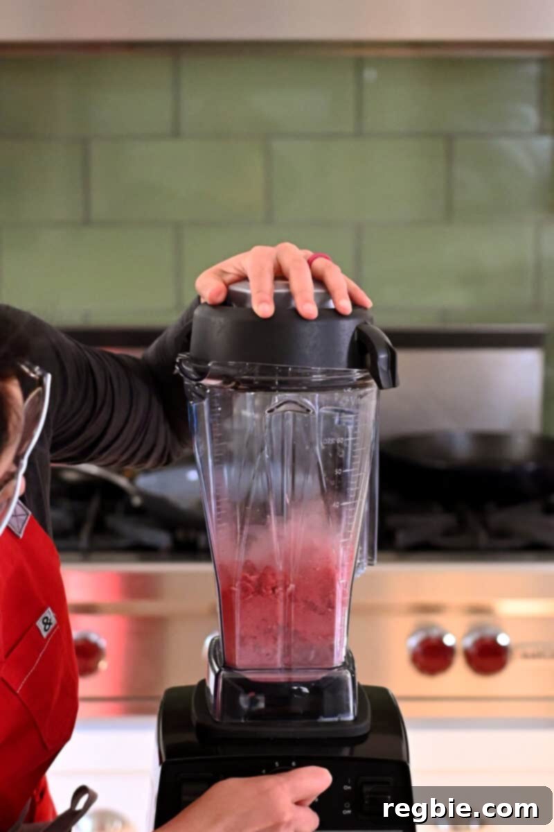 A Vitamix blender actively pulverizing freeze-dried strawberries into a fine, vibrant powder, ready for the cheesecake filling.