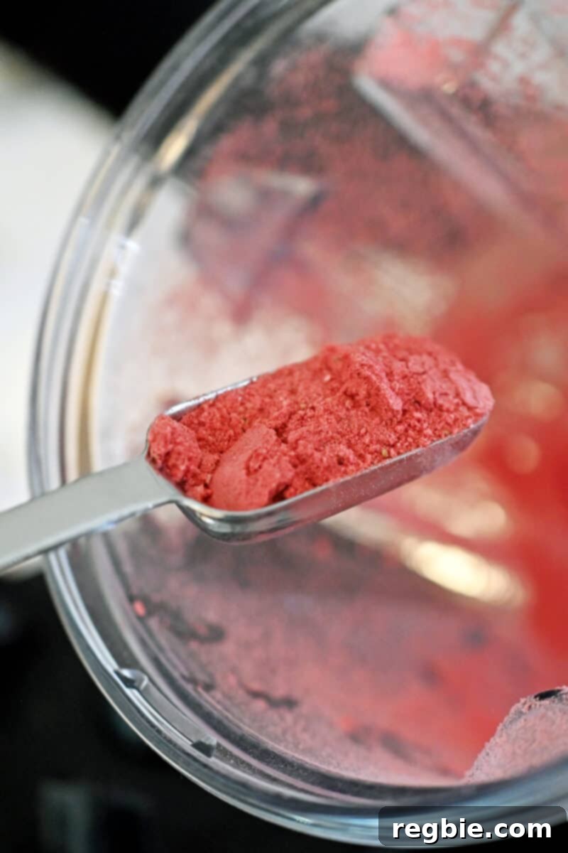A tablespoon of vibrant freeze-dried strawberry powder being scooped out from a blender, to be set aside for later use as a garnish.
