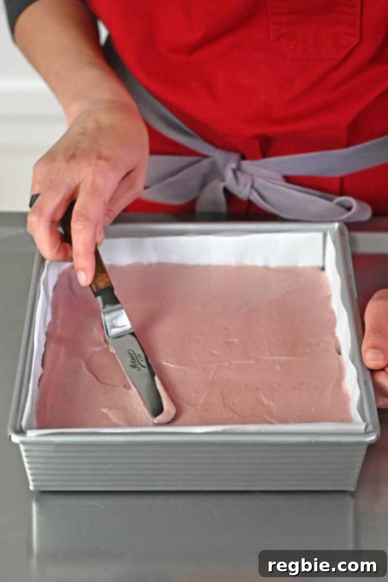 An offset spatula being used to carefully smooth the top surface of the strawberry cheesecake bars, ensuring an even and neat finish.