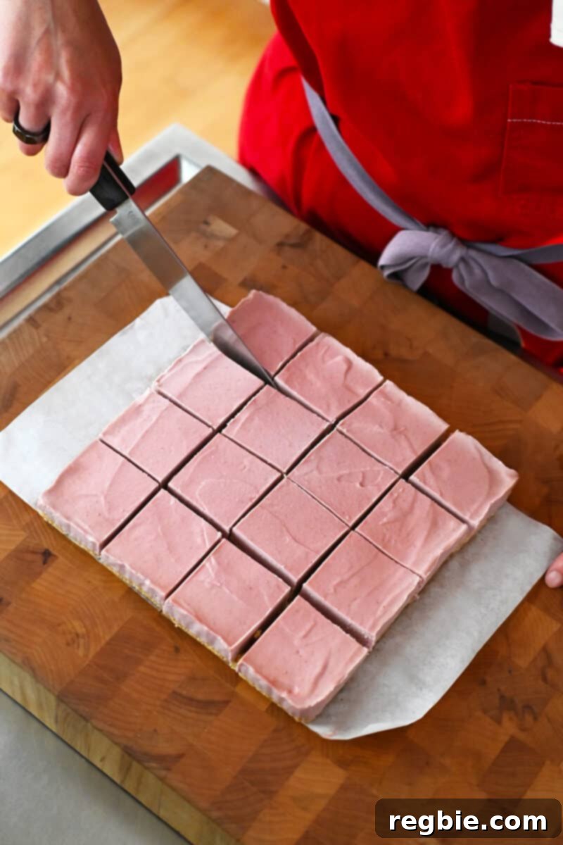 An overhead perspective of a person meticulously cutting a freshly prepared batch of vegan and paleo strawberry cheesecake bars into 16 uniform square pieces.