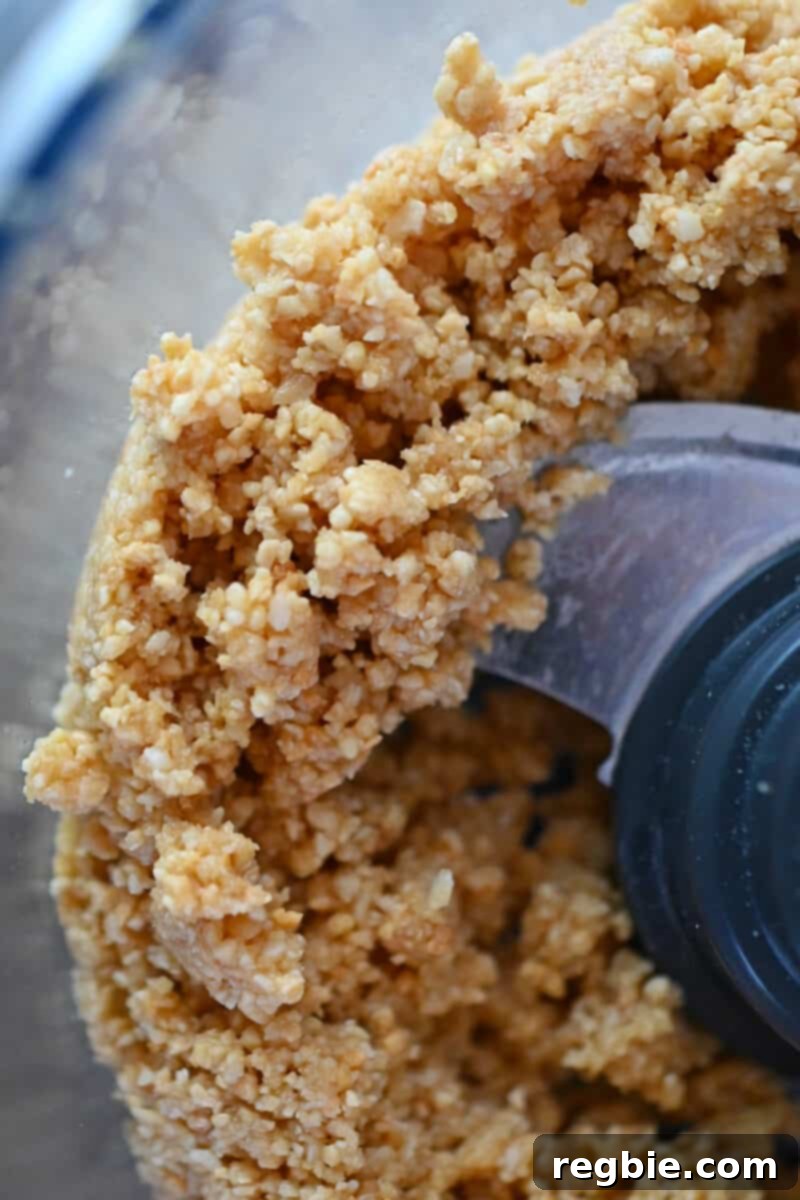 An overhead shot showing the mixed crust ingredients inside an open food processor, now perfectly combined and ready to be transferred to the baking pan.
