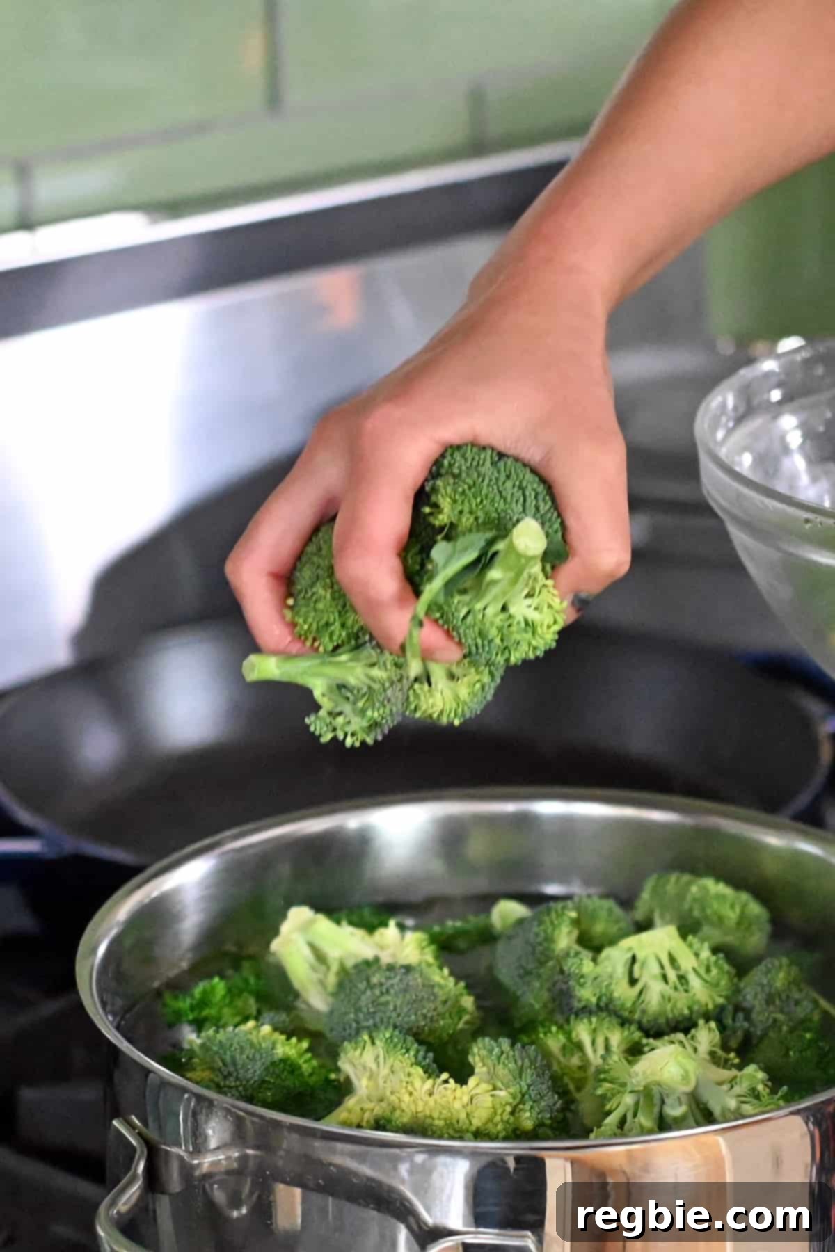 A hand is carefully adding broccoli florets to an open pot of boiling water.