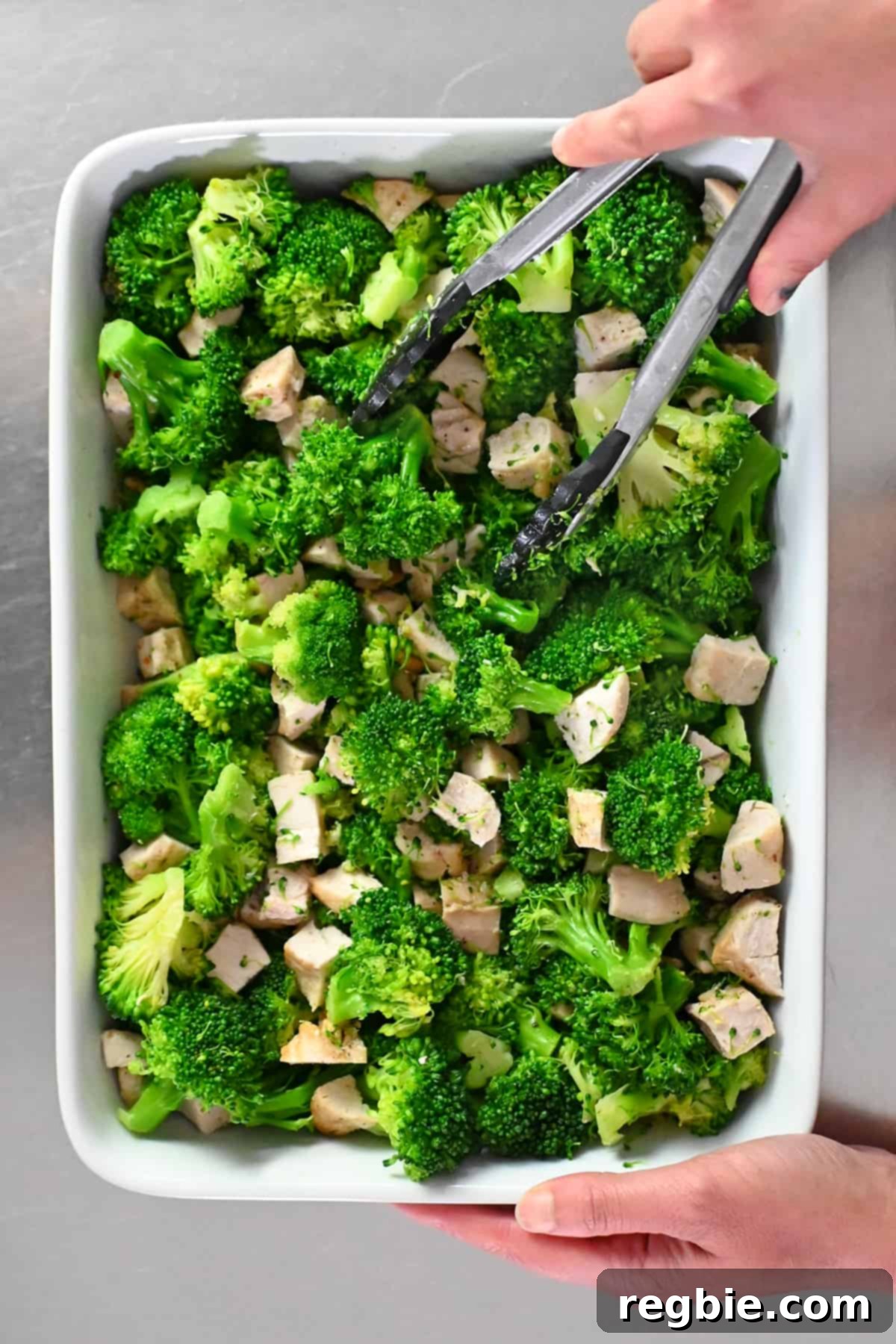 An overhead shot of a white casserole dish filled with seasoned cooked broccoli and cubed chicken, arranged in an even layer.