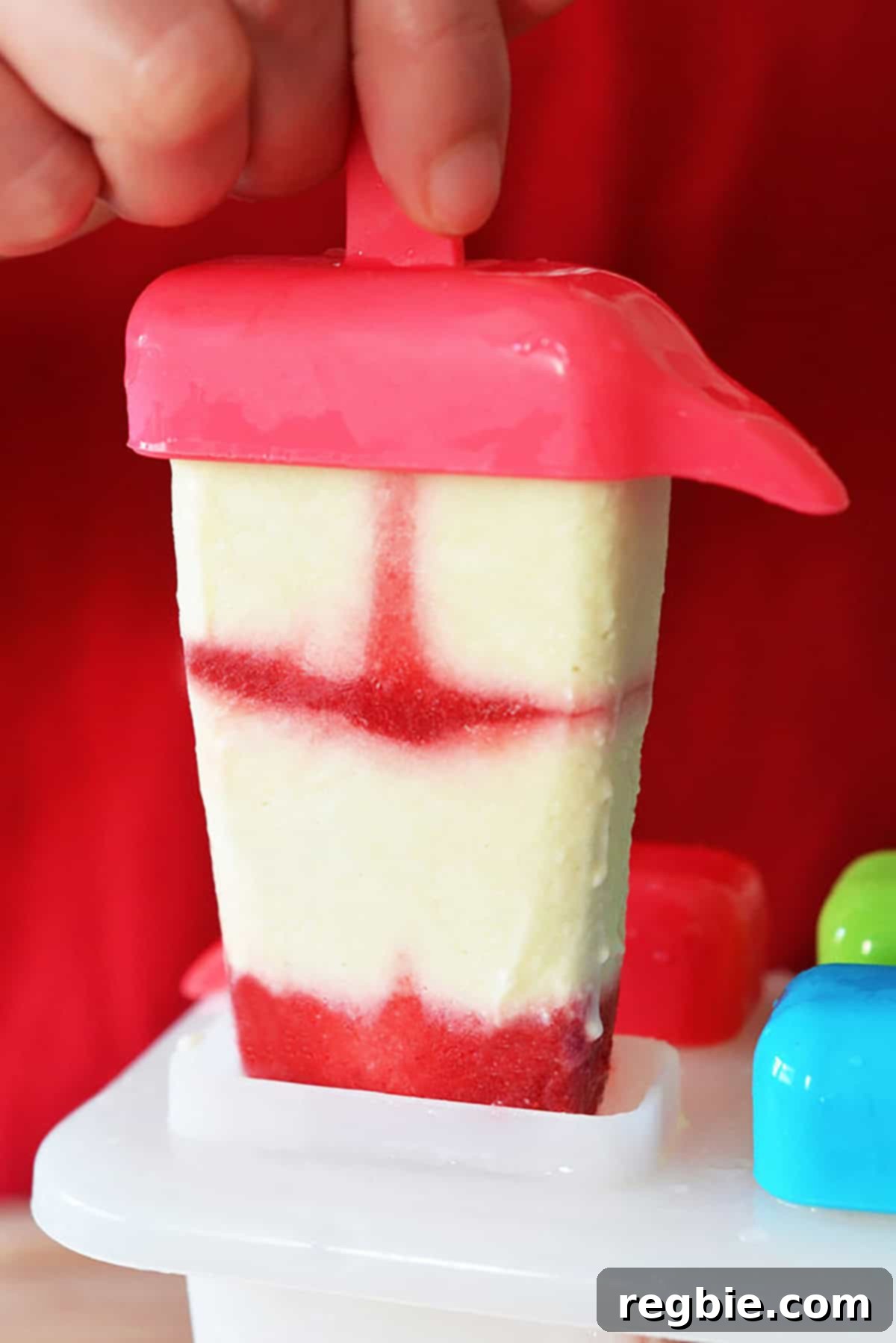 A beautiful red and white swirled lava flow homemade popsicle being pulled out of its mold, perfectly frozen.