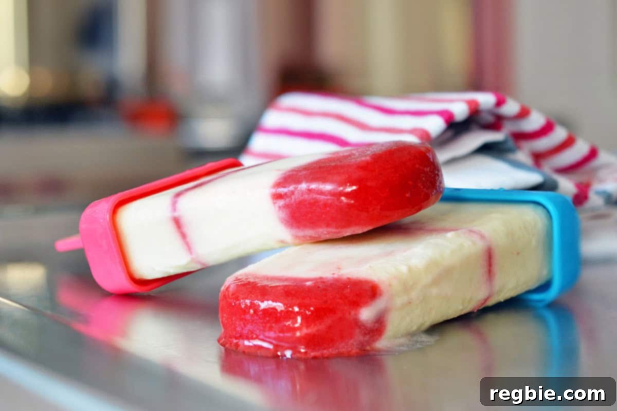 Two vibrant homemade popsicles, red and white, resting askew on a counter, slightly melting in the warm air.