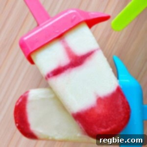 Two red and white homemade popsicles are stacked on top of each other on a wooden surface.