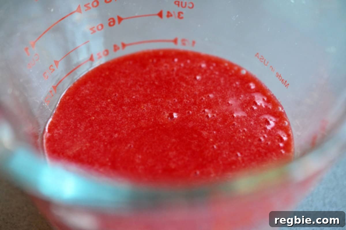 A measuring cup is filled with freshly pureed strawberries, ready for making homemade popsicles.