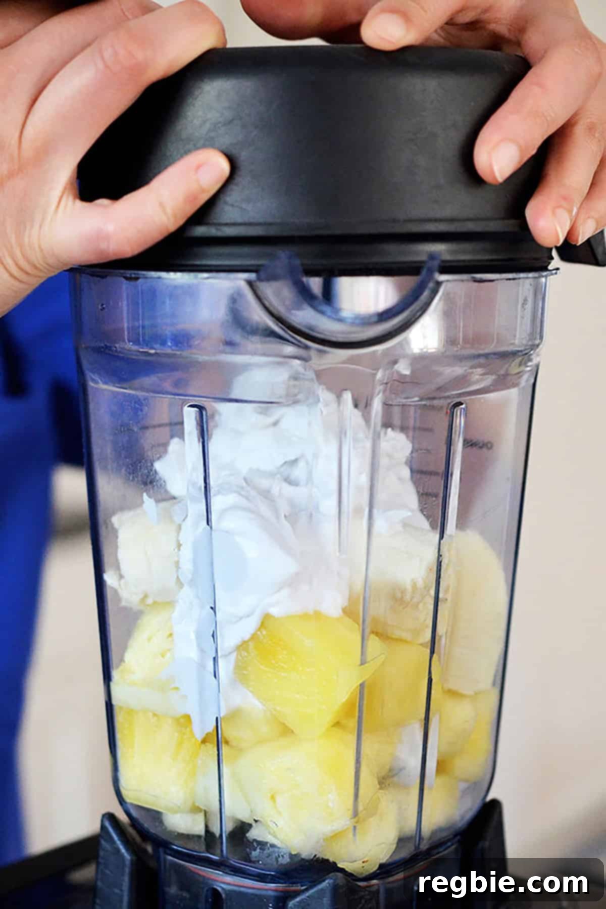 Putting the lid on a blender filled with pineapple chunks, banana slices, and coconut cream, ready to be blended into the creamy base.