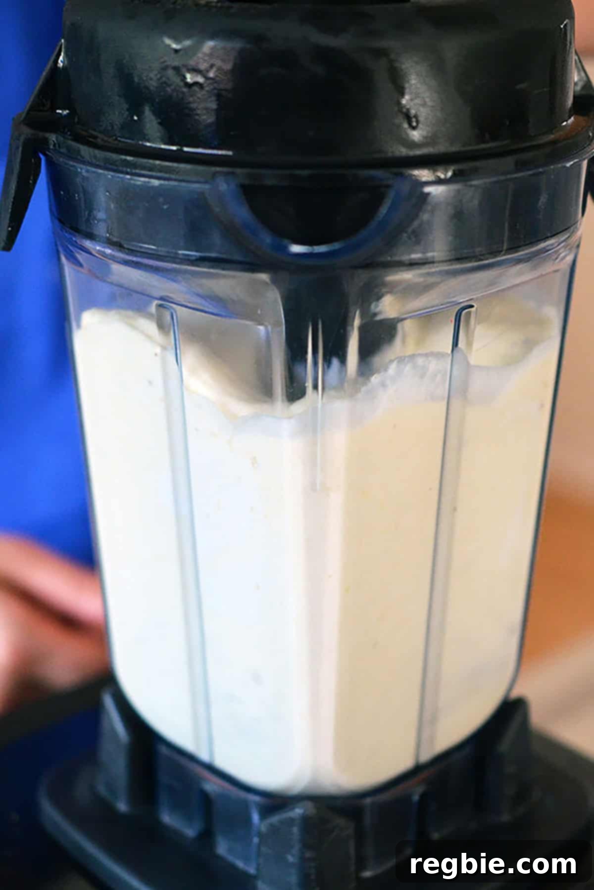 A side view of a blender filled with a smooth, creamy white liquid, indicating the perfectly blended piña colada base.