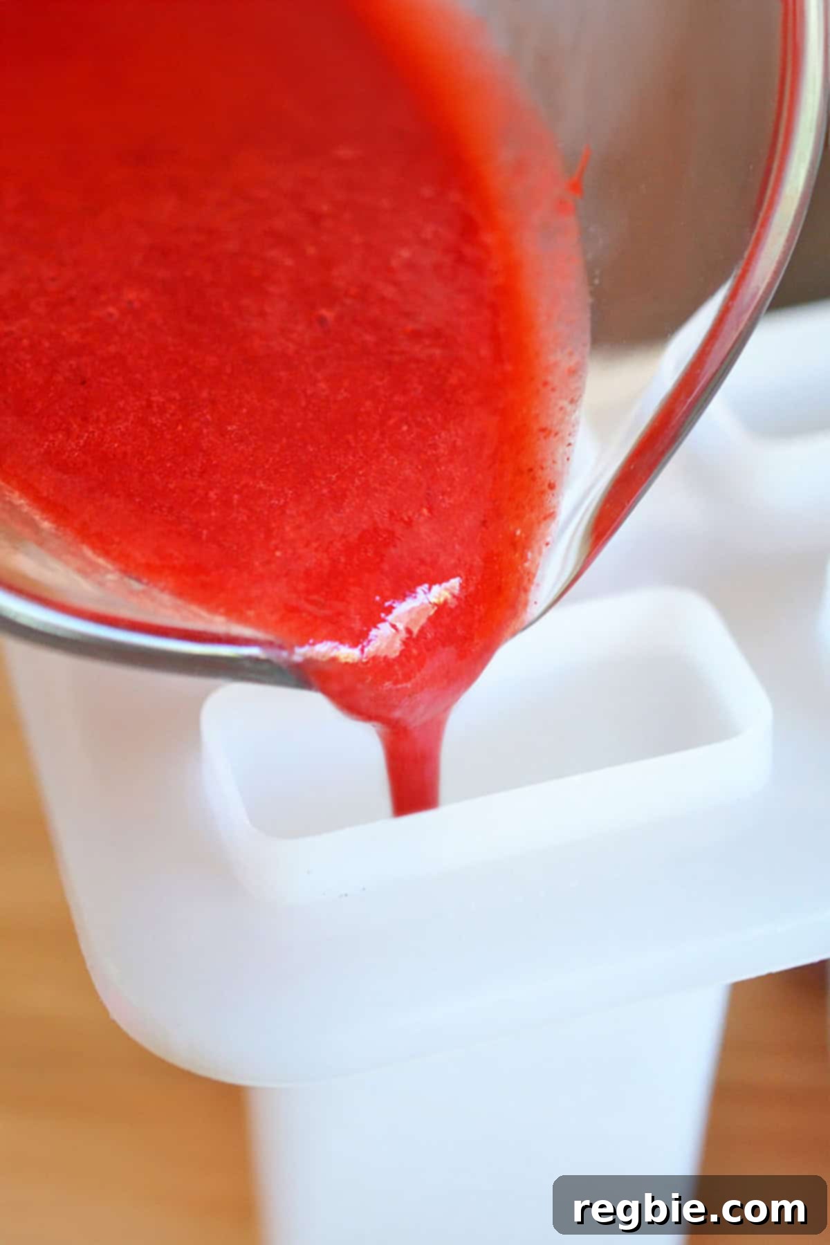 Carefully pouring strawberry puree into the bottom of a popsicle mold to start the layering process.