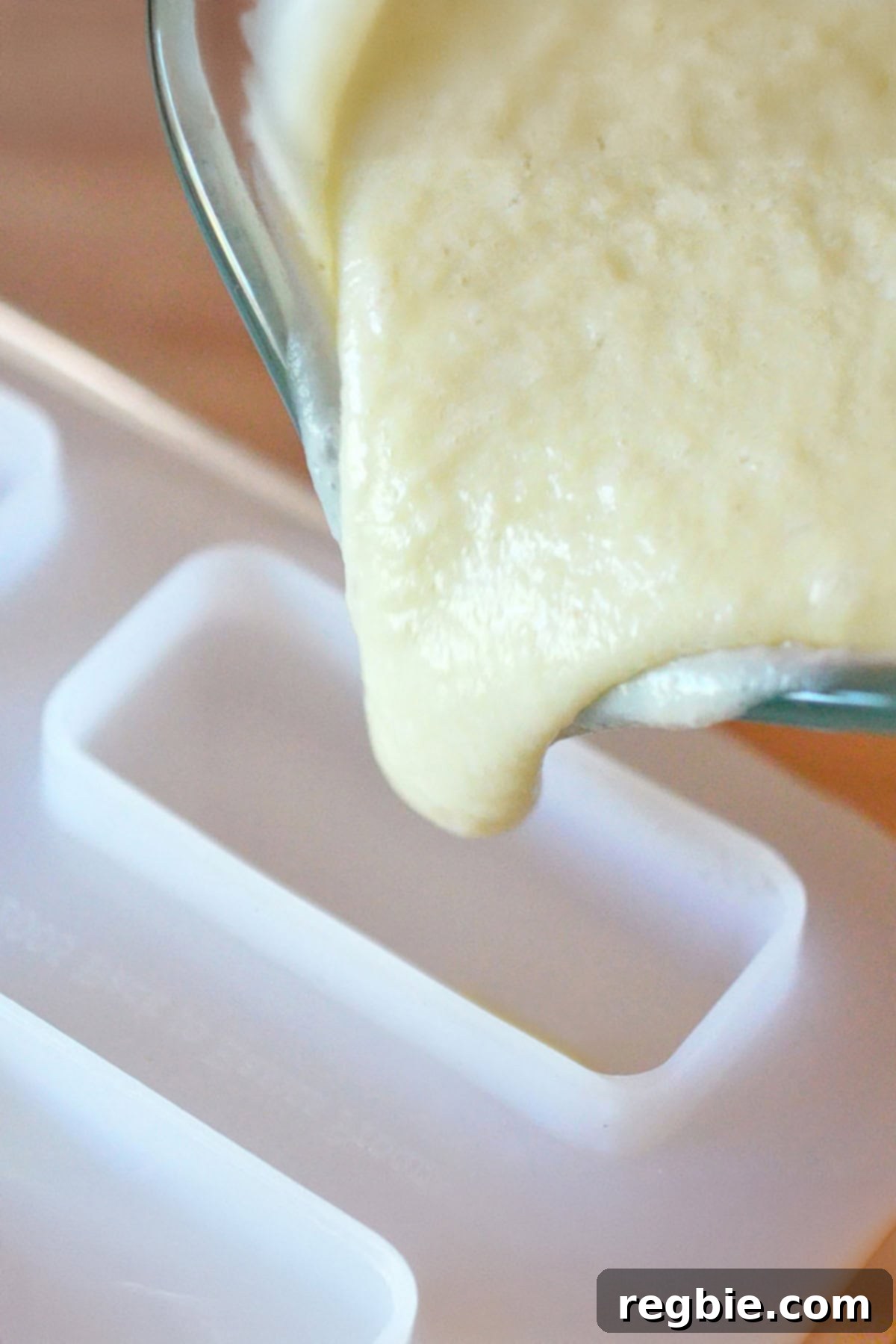 Pouring the piña colada portion of the lava flow popsicle mixture into the mold, filling it partially.