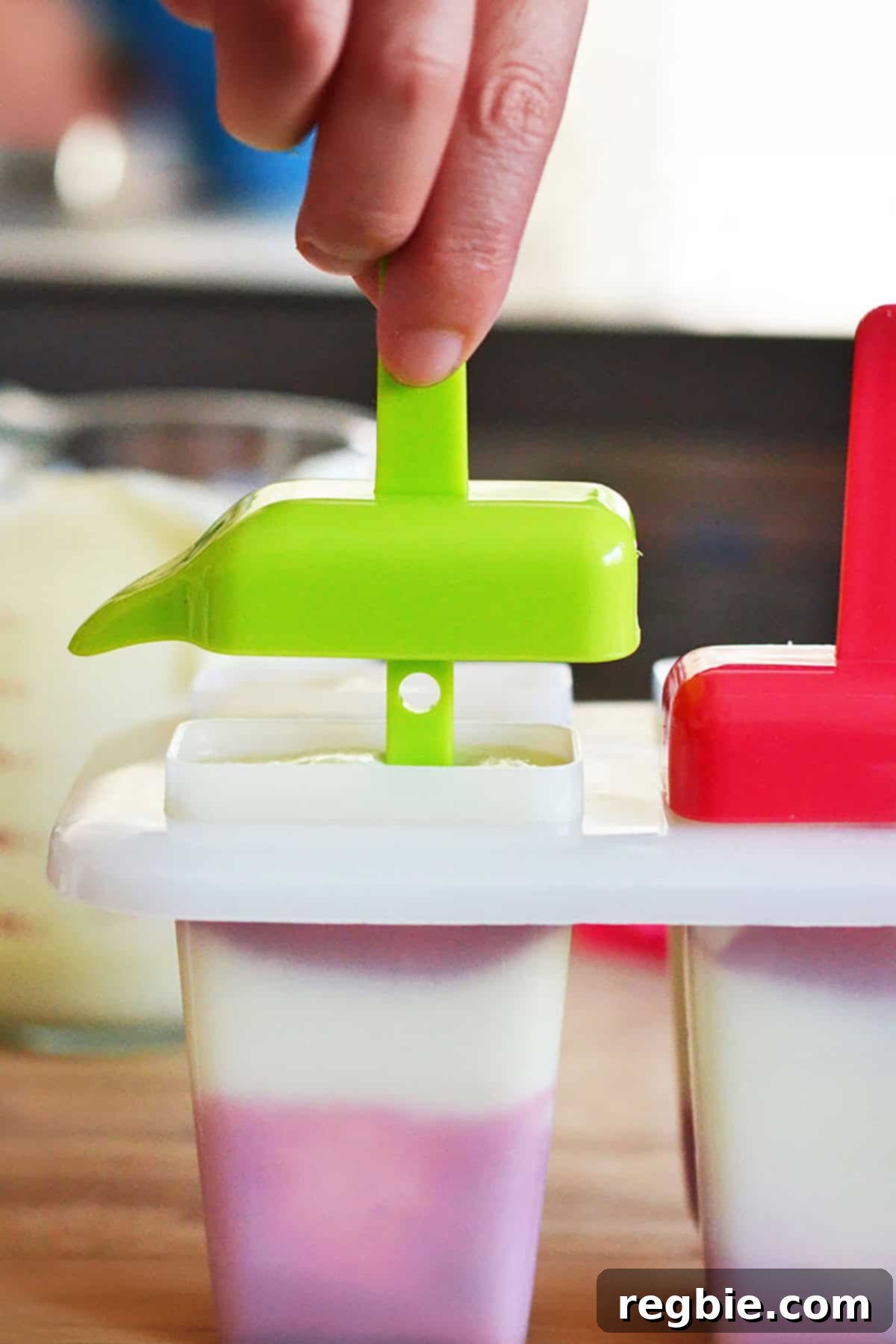 Inserting the popsicle stick into the mold filled with lava flow mixture, preparing for freezing.