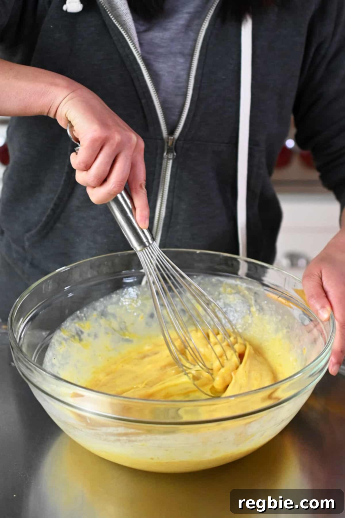 A close-up shot of a whisk combining eggs, almond milk, nutritional yeast, and seasonings in a large mixing bowl for the dairy-free and paleo quiche filling.