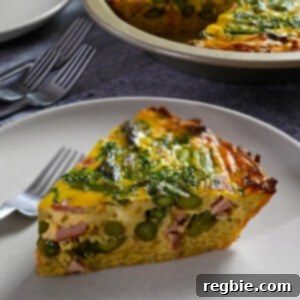 A slice of paleo and dairy free asparagus quiche on a plate in front of pie pan with quiche inside.