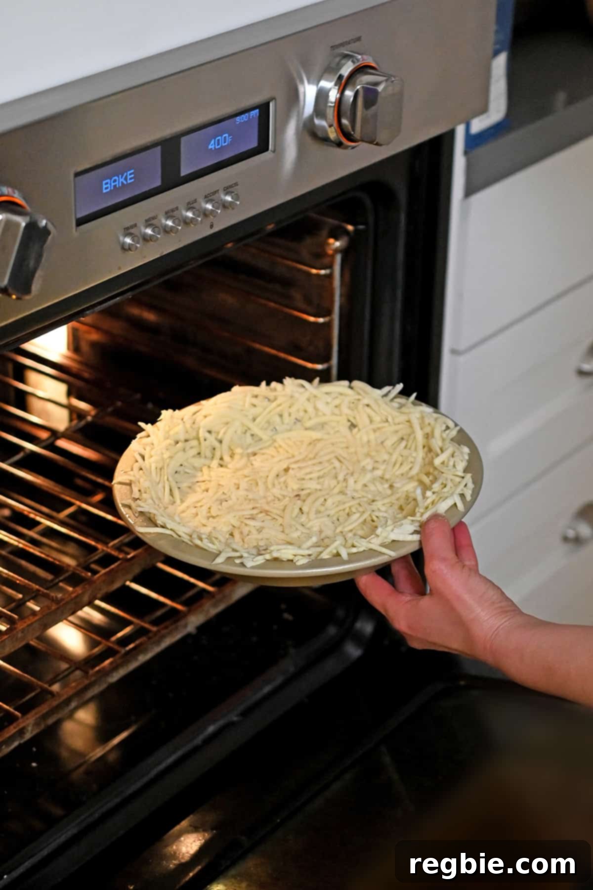 A pie plate containing the shredded potato crust being carefully placed into a hot oven for par-baking.