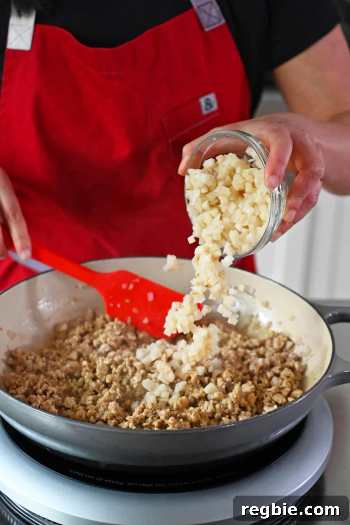 Adding a bowl of diced water chestnuts to a skillet with cooked chicken in a brown sauce.