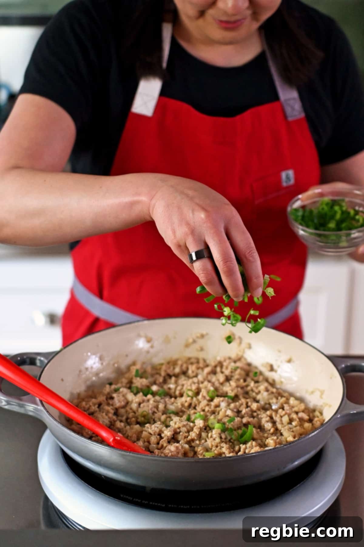 Sprinkling sliced green onions into a skillet filled with ground chicken lettuce wrap filling.