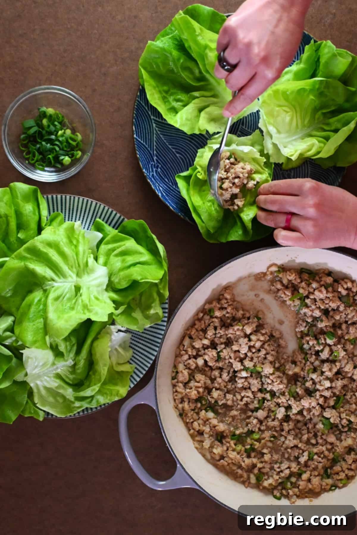 An overhead shot of someone adding a spoon full of chicken filling inside a lettuce wrap.