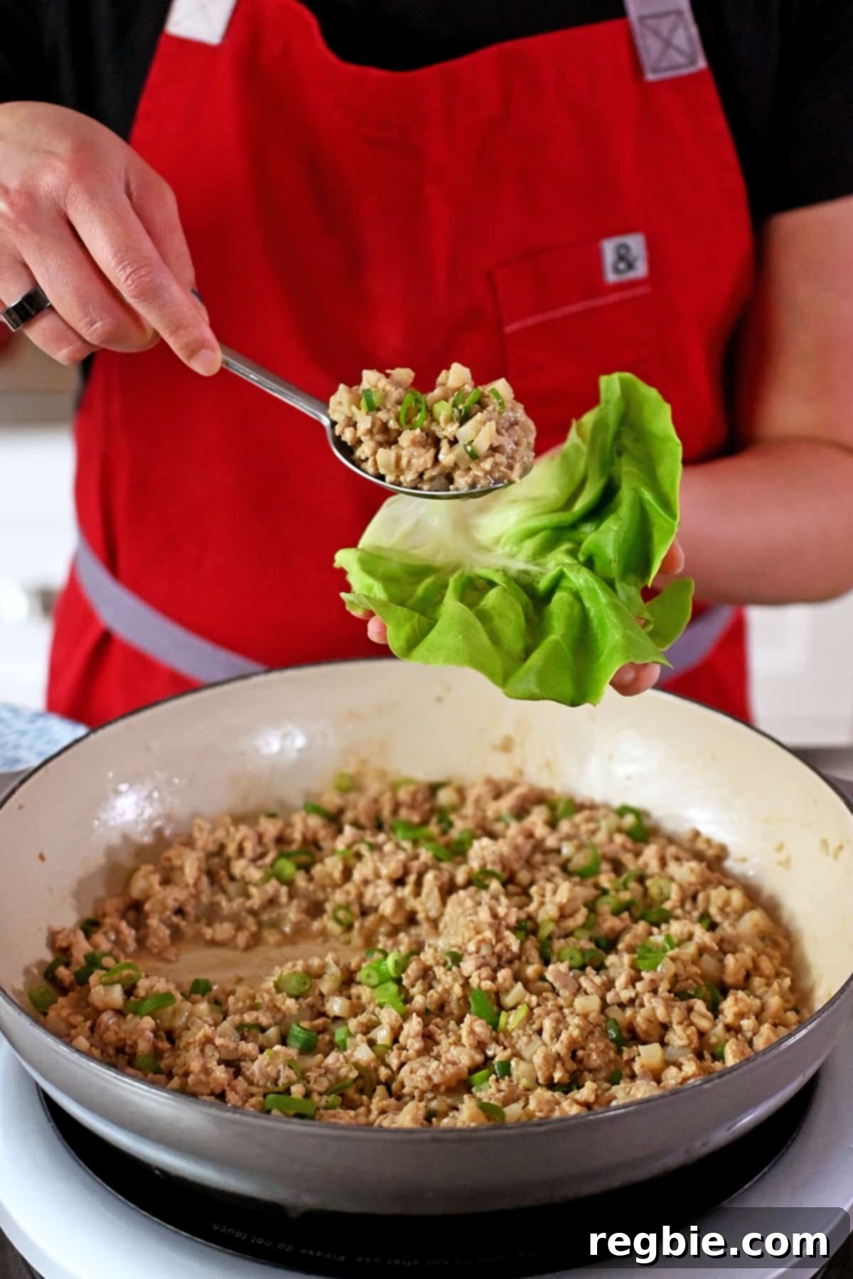 Spooning seasoned ground chicken from a skillet into a crisp lettuce leaf.