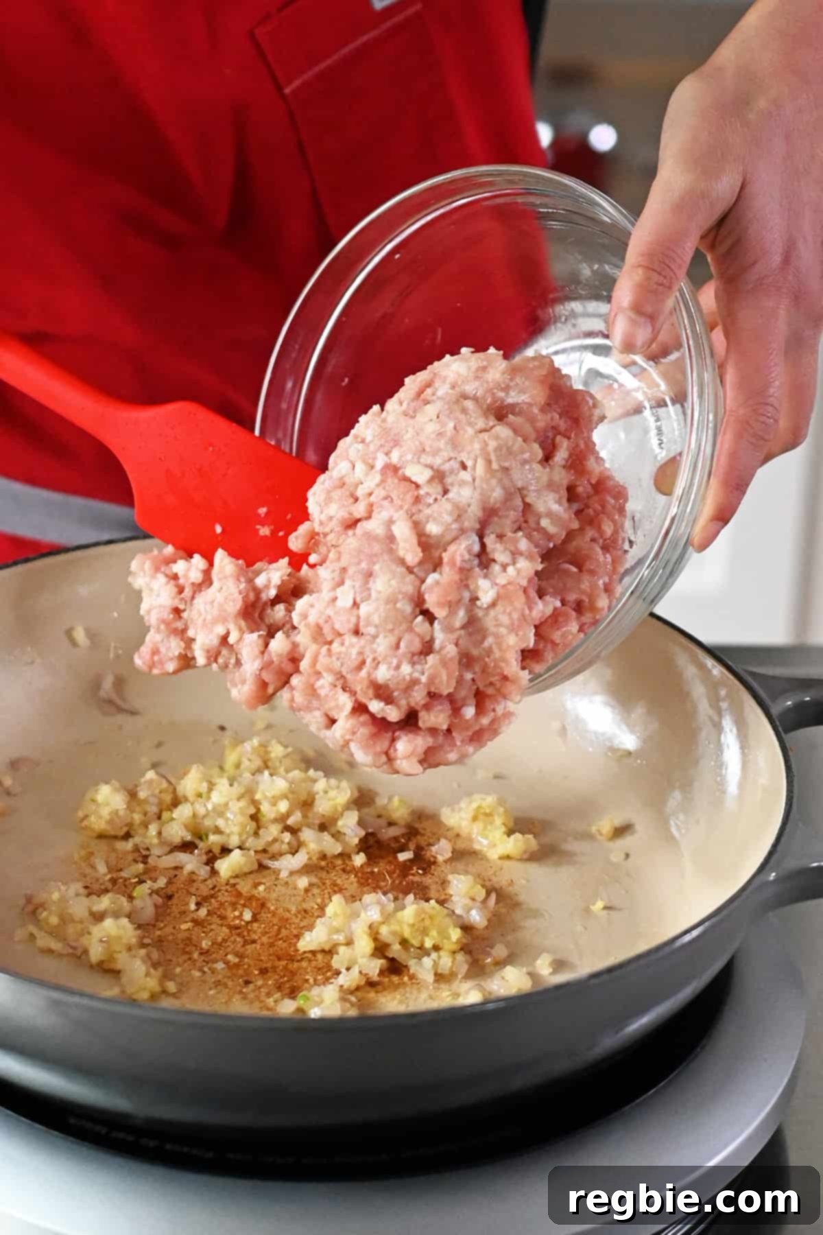 Adding raw ground chicken to a skillet with minced shallots, garlic, and ginger.