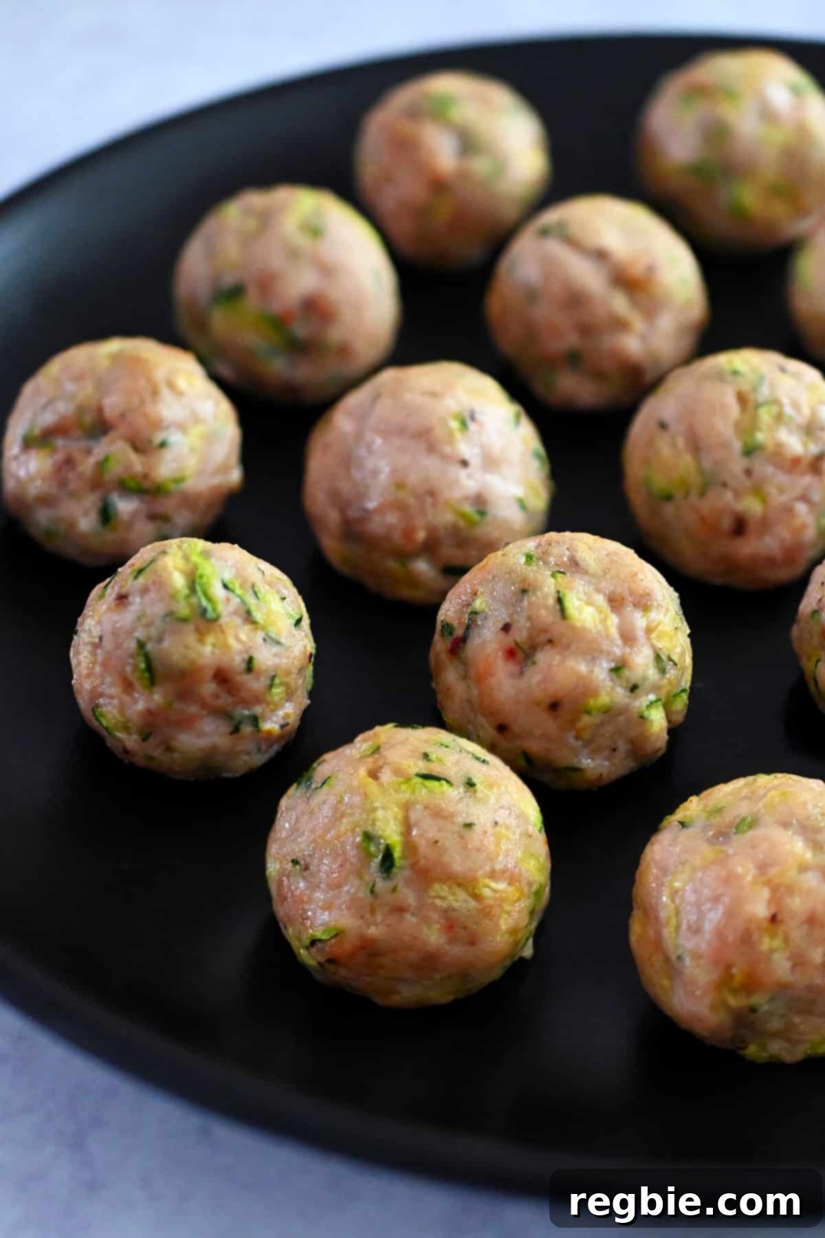 A black plate topped with succulent paleo baked chicken meatballs, garnished with fresh herbs and made with shredded zucchini for extra moisture.