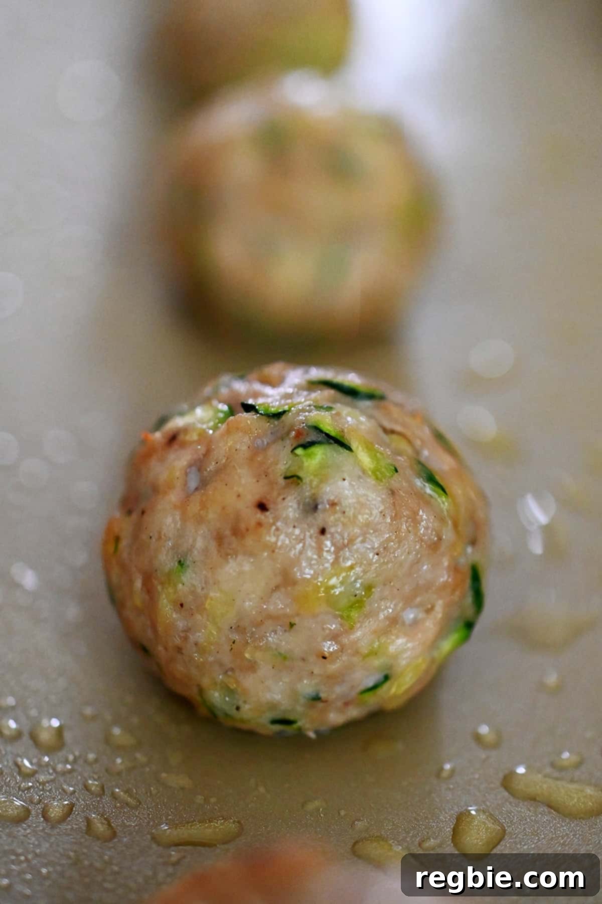 A close-up shot of a perfectly cooked chicken meatball, fresh out of the oven, showcasing its golden-brown exterior and tender texture.