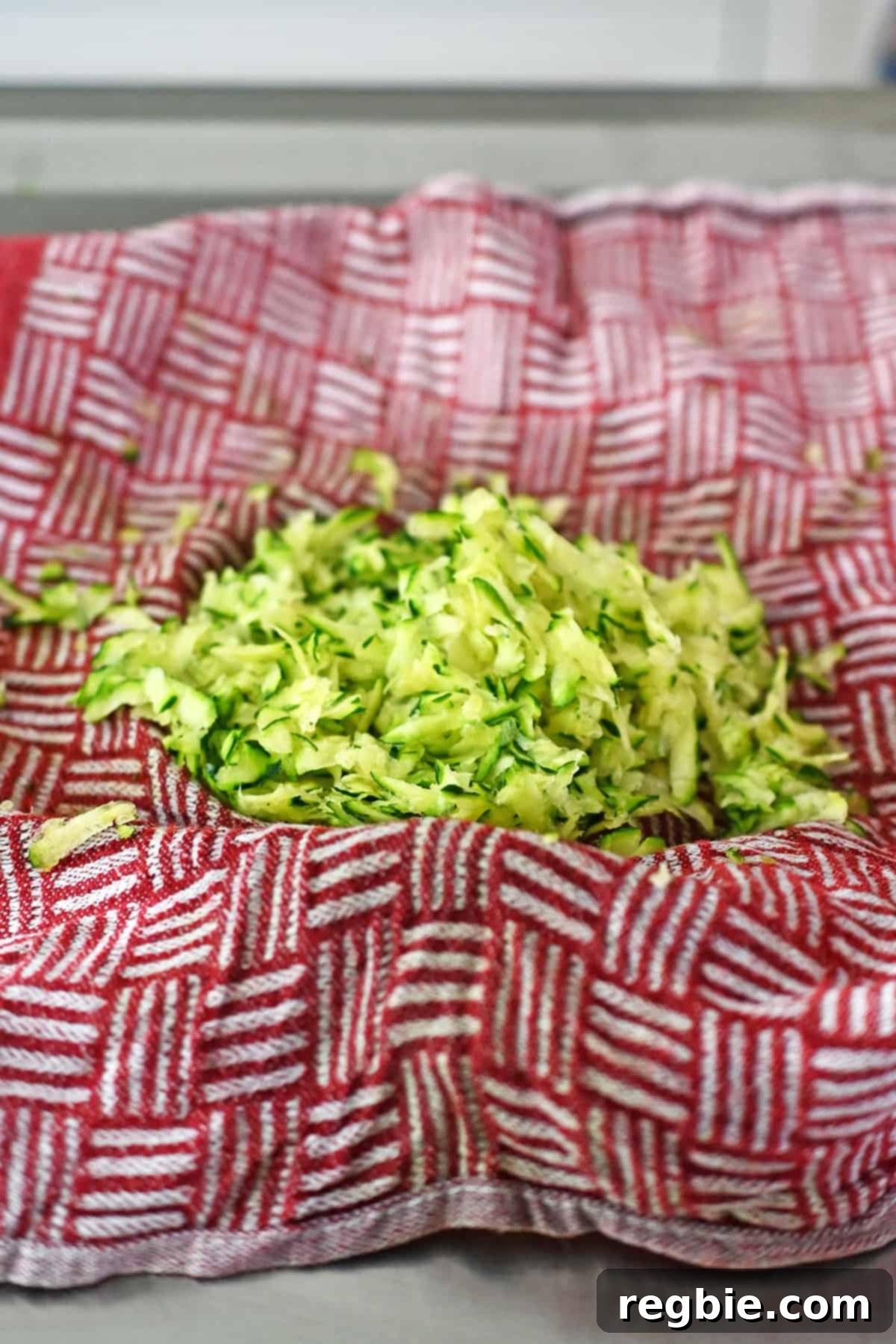 A close-up view of freshly shredded zucchini, thoroughly squeezed dry and collected in a red and white kitchen towel, ready for mixing into chicken meatballs.