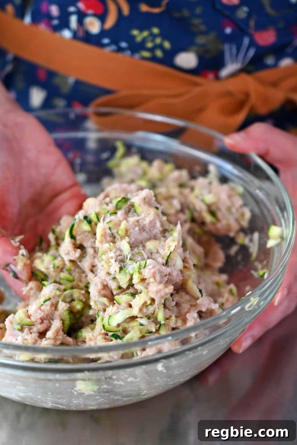 A pair of clean hands gently mixing the chicken meatball mixture in a glass bowl, ensuring all ingredients are well combined without overworking the meat.