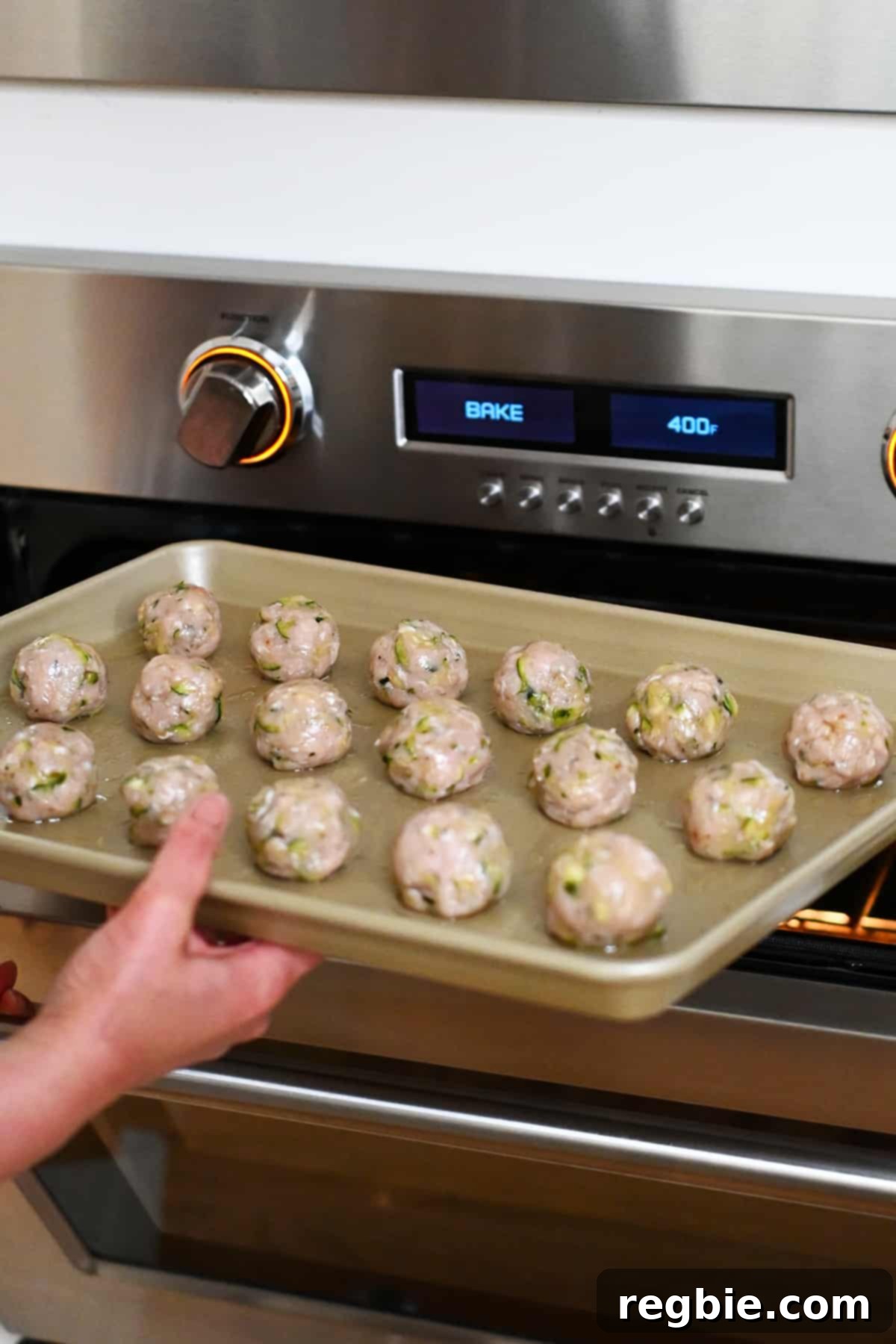 A baking tray filled with perfectly portioned chicken meatballs being carefully placed into a preheated 400°F oven, ready for baking.