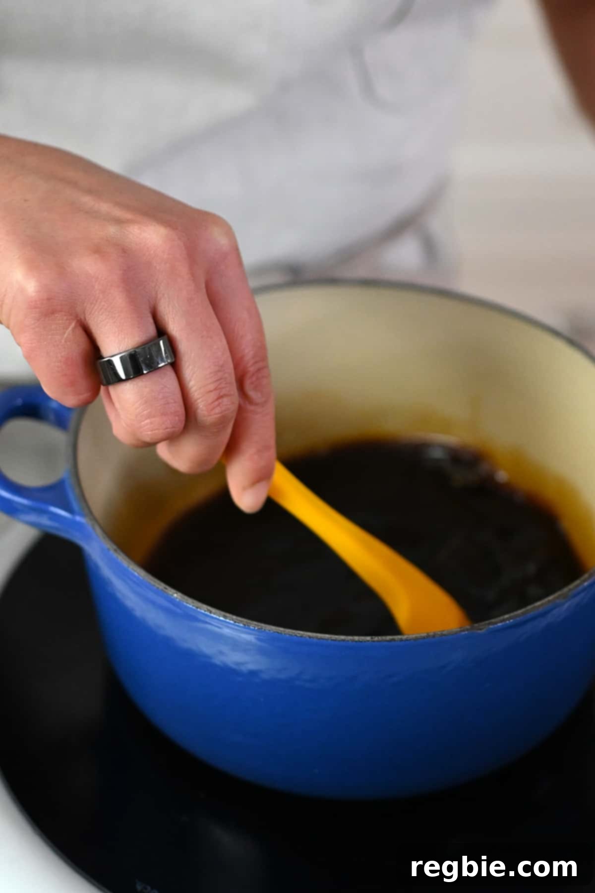 Stirring paleo and Whole30 teriyaki sauce in a small saucepan with a yellow silicone spatula.