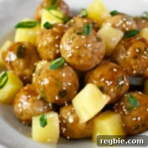 A side view of a plate of teriyaki pineapple chicken meatballs with cubed pineapple.